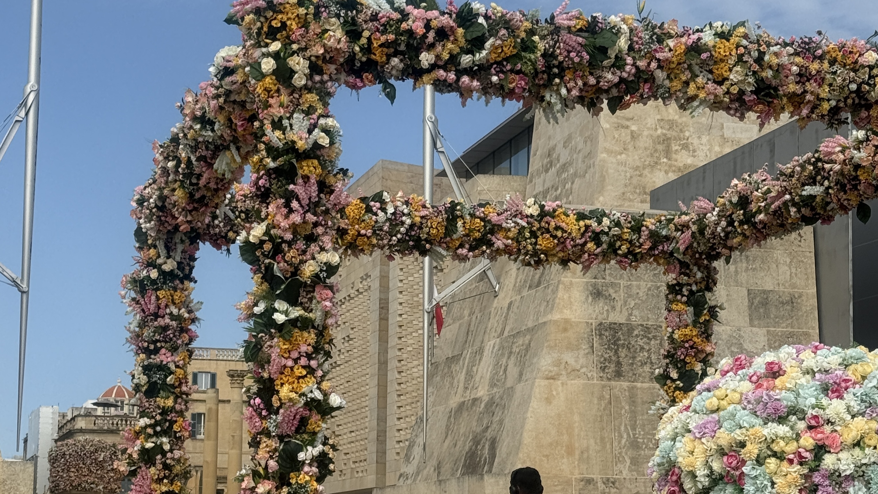 Close detail of a floral installation arch at Valletta Green Festival against Maltese limestone architecture.