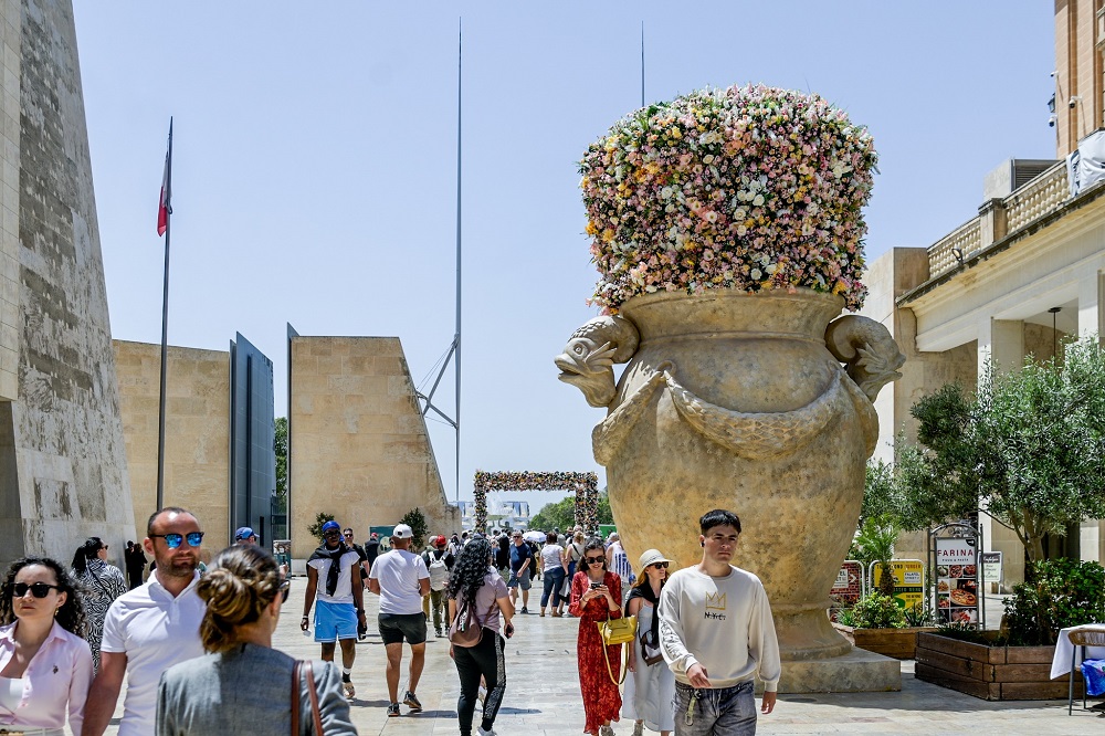 Large floral urn installation at Valletta Green Festival with visitors passing through the city entrance.